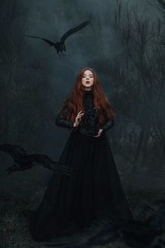 a woman with long red hair in a black dress and two crows flying over her