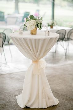 a white table topped with a vase filled with flowers on top of a table covered in cloth