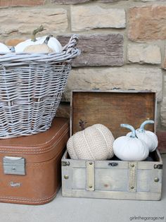 two suitcases with white pumpkins in them sitting next to a basket and brick wall