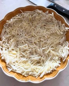 a bowl filled with shredded cheese next to a knife