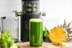 a green smoothie sitting on top of a wooden cutting board next to an open juicer