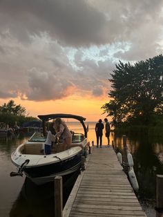 two people are standing on the dock next to a small boat as the sun sets