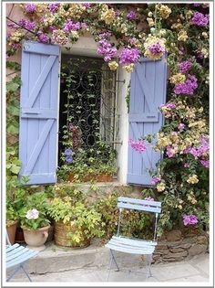 an open window with blue shutters and purple flowers on the wall next to two chairs