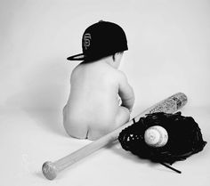 a black and white photo of a baby with a baseball bat, glove and ball