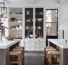 an open kitchen with white cabinets and wooden stools in the center, filled with dishes