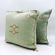 two green pillows with embroidered designs on them sitting next to each other in front of a white background