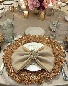 the table is set with silver and gold place settings, napkins, and flowers