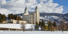 a large building with two towers in the middle of a snow covered field and mountains behind it