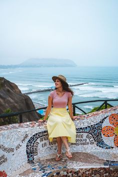 a woman sitting on top of a mosaic wall next to the ocean in front of a beach