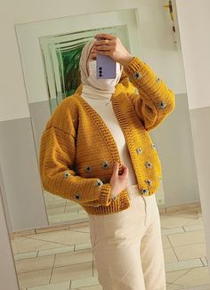 a woman taking a selfie in front of a mirror wearing a yellow sweater and beige pants