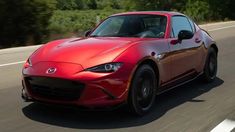 a red mazda sports car driving down the road with trees in the backgroud