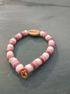 a pink and white beaded bracelet with a gold plated charm on it's end