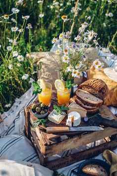 an outdoor picnic with bread, orange juice and fresh fruit on the table in front of some daisies