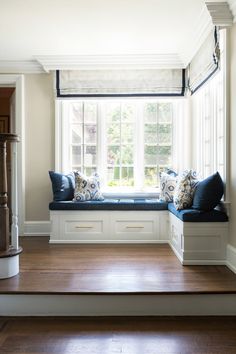 a window seat with pillows on it in front of a wooden floor and white walls