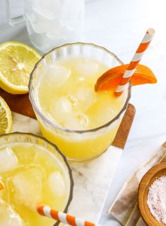 two glasses filled with lemonade sitting on top of a counter next to sliced oranges