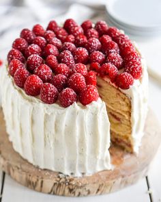 a cake with white frosting and raspberries on top sitting on a wooden board