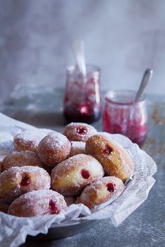 powdered sugar covered donuts in a white bowl on a table next to jam jars