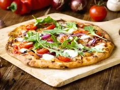 a pizza sitting on top of a wooden cutting board next to tomatoes and other vegetables