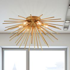 a modern light fixture hanging from the ceiling in a living room with large windows and white walls