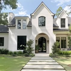 a white house with black windows and steps leading up to the front door that leads into the yard