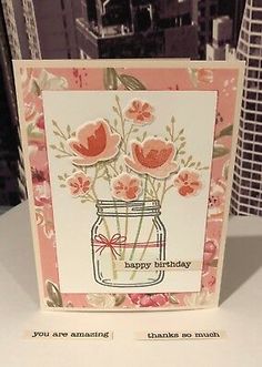 a birthday card with flowers in a mason jar on top of a table next to a cityscape