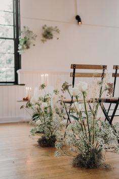 white flowers and greenery are arranged in vases on the floor next to chairs