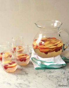 four glasses and pitcher filled with liquid sitting on a marble counter top next to each other