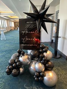 an arrangement of silver and black balloons in the middle of a carpeted area with a sign on top