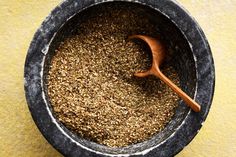 a wooden spoon in a black bowl filled with granola on a yellow tablecloth