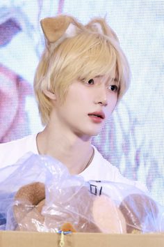 a young man with blonde hair holding a teddy bear in a cardboard box on stage