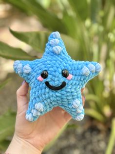 a hand holding up a blue crocheted star with a smiley face on it