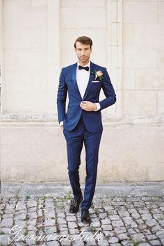 a man in a blue tuxedo and bow tie standing on cobblestone