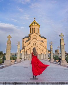 a woman in a red dress is walking towards a church with statues on either side