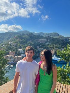 a man and woman standing next to each other on top of a hill near the ocean