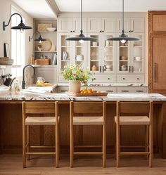 a large kitchen with wooden cabinets and marble counter tops, along with two stools in front of the island