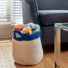 a basket full of yarn sitting on the floor next to a couch