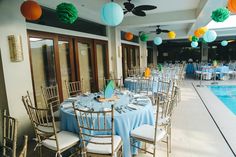 tables set up for an event with paper lanterns hanging from the ceiling and blue tablecloths