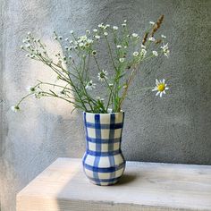 a blue and white checkered vase with daisies in it sitting on a ledge