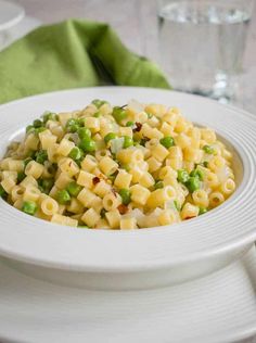 a white bowl filled with macaroni and peas on top of a table next to a green napkin