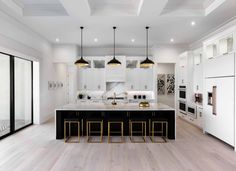 a large kitchen with white cabinets and black counter tops, gold bar stools and pendant lights