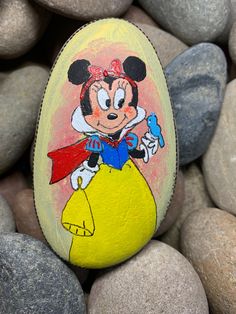 a painted rock with an image of minnie mouse on it, surrounded by some rocks