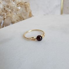 * Garnet Round Gemstone Bead, 4mm * 14/20 gold-filled (5%) with jeweler's brass core, 1.6 mm round wire * Refer to the ring size guide in the photos above for a perfect fit. * Arrives beautifully packaged, ideal for gifting yourself or a loved one. * Easy care instructions in the photos above that ensure long-lasting beauty. * A jewelry care card and cleaning cloth are included. Adorn your style effortlessly with a handcrafted wire wrapped ring. This piece of jewelry combines the enduring allure Handmade Adjustable Minimalist Birthstone Ring, Handmade Minimalist Adjustable Birthstone Ring, Minimalist Gold Birthstone Ring With Gemstone, Minimalist Adjustable Gold Birthstone Ring, Handmade Dainty 14k Gold Birthstone Ring, Minimalist Amber Birthstone Jewelry, Minimalist Wire Wrapped Yellow Gold Ring, Minimalist 14k Gold Wire Wrapped Rings, Minimalist Amber Ring Jewelry