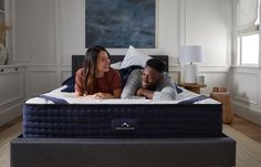 a man and woman laying on top of a blue mattress in a room with white walls