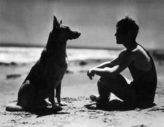 a man kneeling down next to a dog on the beach