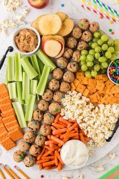 a platter filled with crackers, carrots, celery, grapes, apples, and other snacks