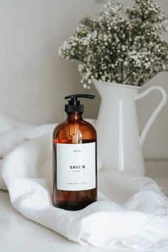 a bottle of soap sitting on top of a white cloth next to a vase with flowers