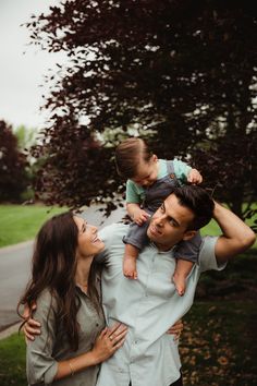 a man and woman holding a baby in their arms while standing next to a tree