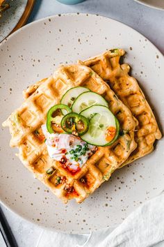 a waffle topped with cucumbers and other toppings on a white plate