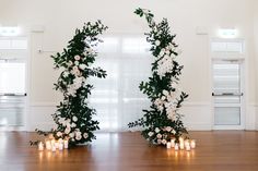 two floral archways with candles on the floor in front of them are decorated with white flowers and greenery