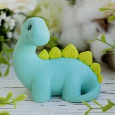 a blue toy dinosaur sitting on top of a table next to some flowers and cotton